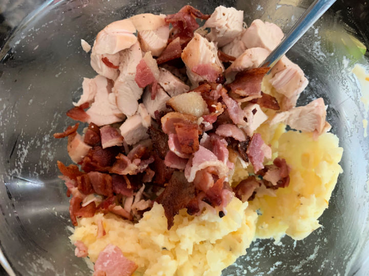 Adding potato, chicken, cheese, and bacon in a bowl.