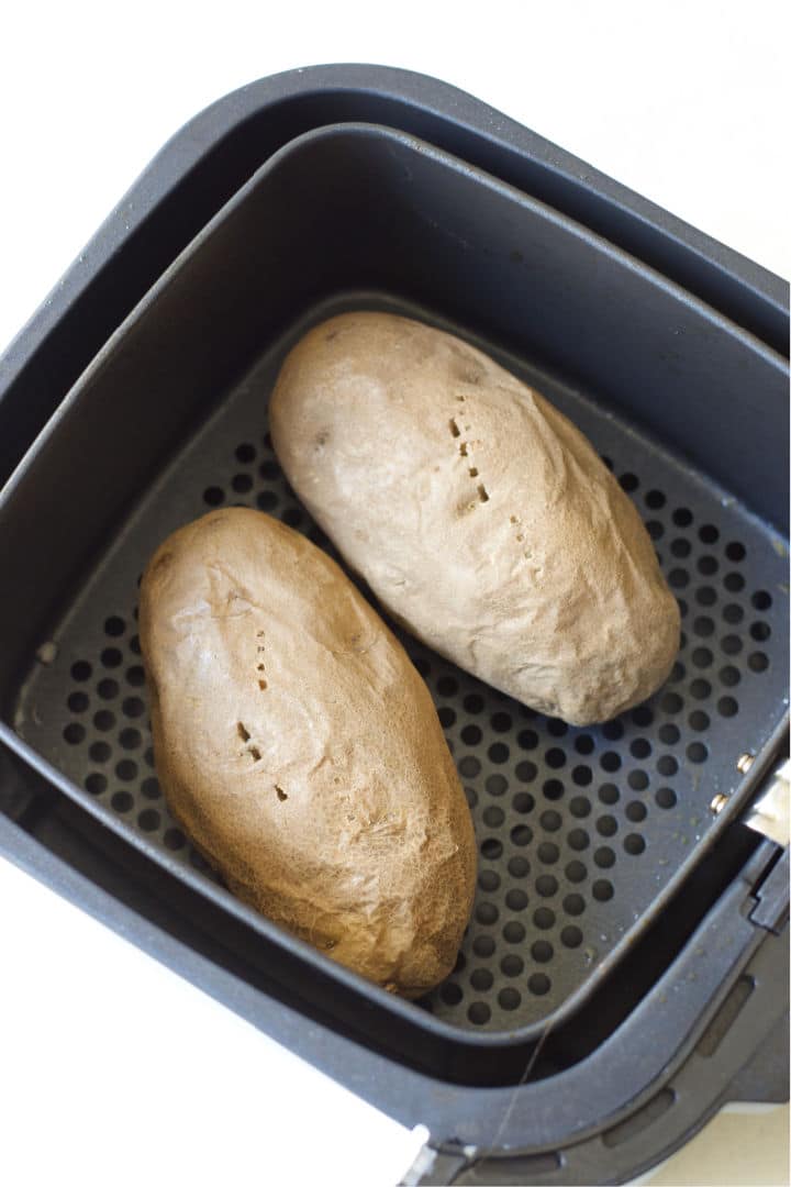 Two cooked baked potatoes in the air fryer.