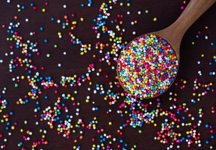 A wooden spoon filled with rainbow colored circle sprinkles.