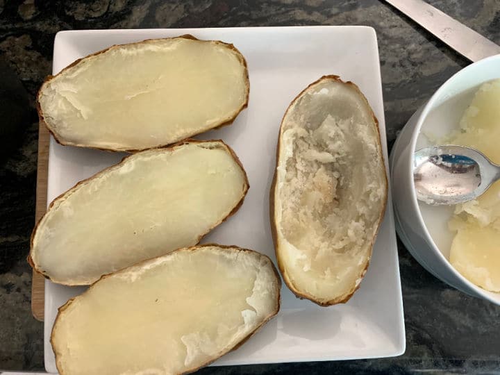 Baked Potatoes cut in half on a plate. One has the insides scooped out.