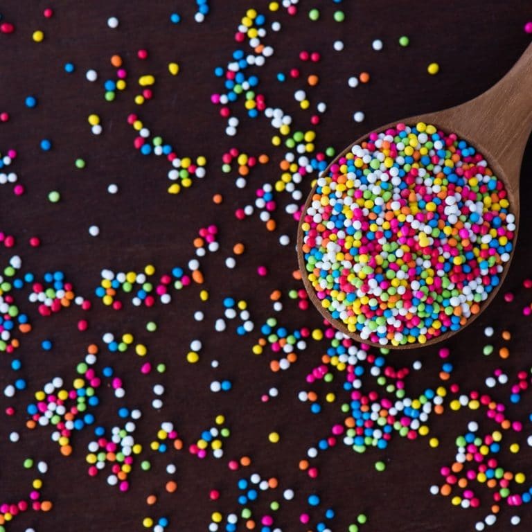 a wooden spoon full of little ball shaped rainbow sprinkles