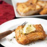 a slice of cod on a white plate. The serving dish of cod is in the background