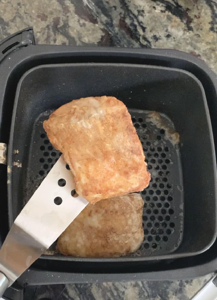 A spatula lifting a piece of cod out of the air fryer.