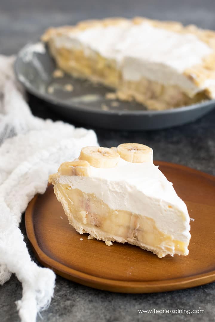 A slice of banana cream pie on a wooden plate.