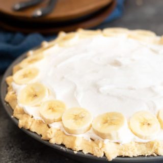 A whole banana cream pie with wooden plates behind the pie.