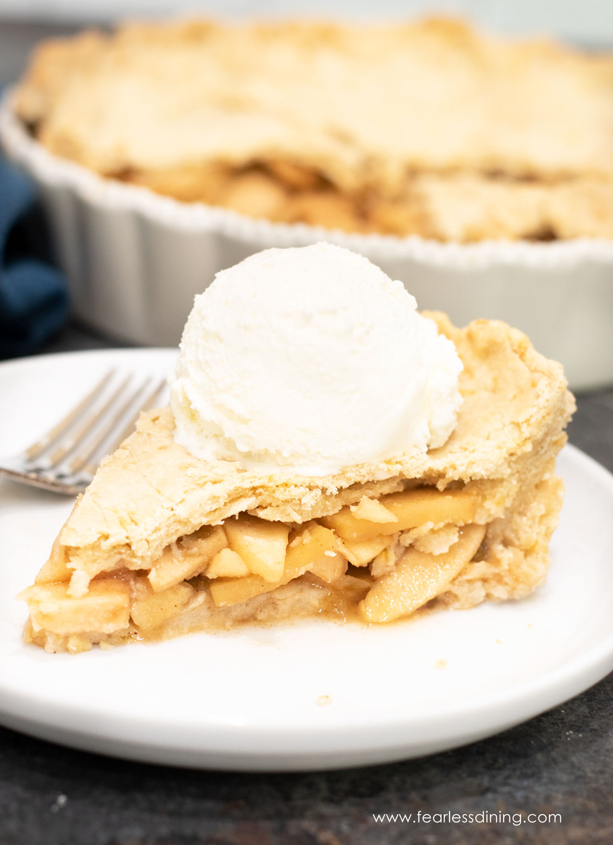 A slice of gluten free hatch chile apple pie on a plate. The slice is topped with a scoop of vanilla ice cream