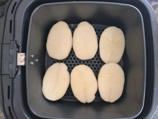 Potato halves in an air fryer basket.