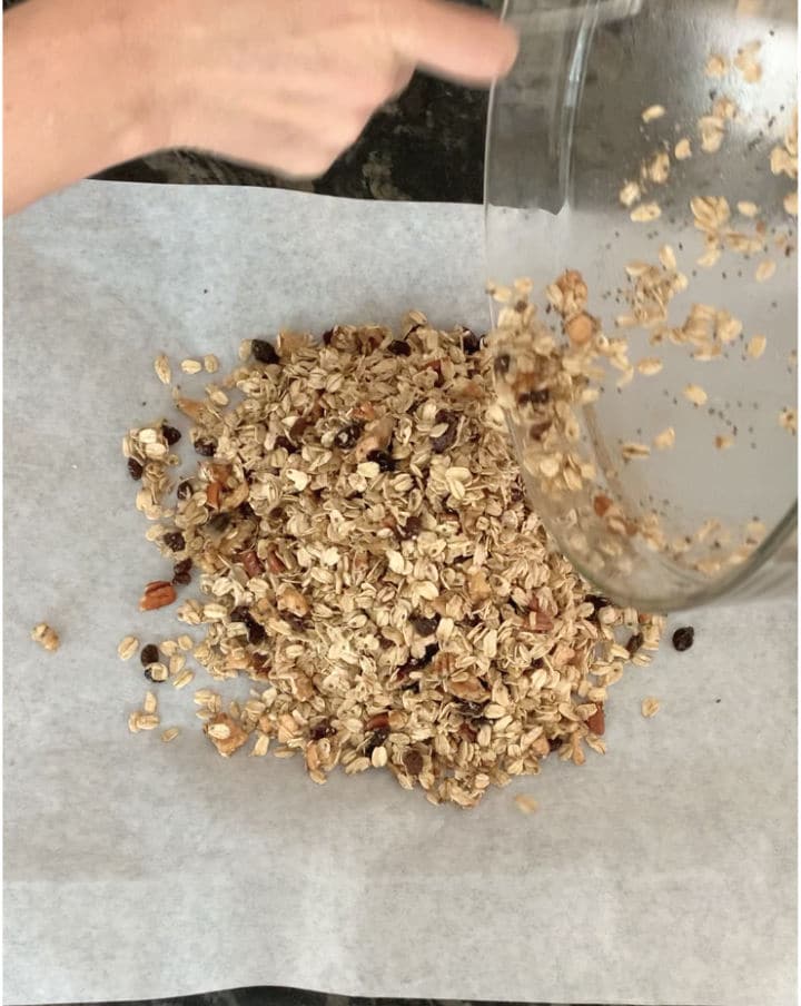 Using a spoon to dump the granola mixture on a parchment paper lined cookie sheet.