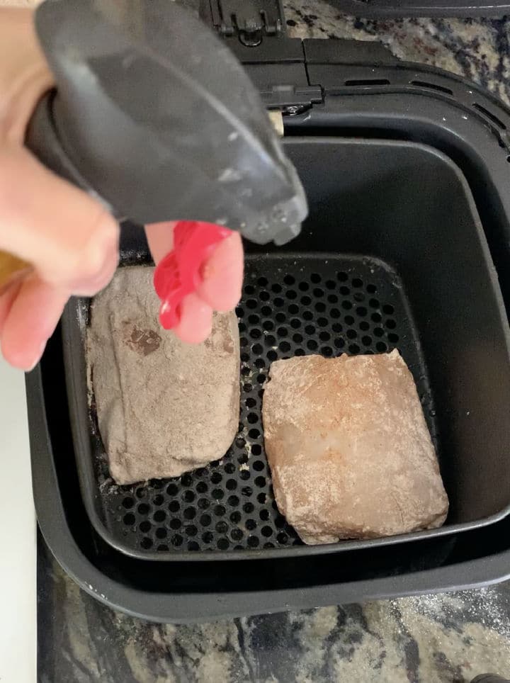 Using an oil sprayer to spray the seasoned cod in the air fryer.