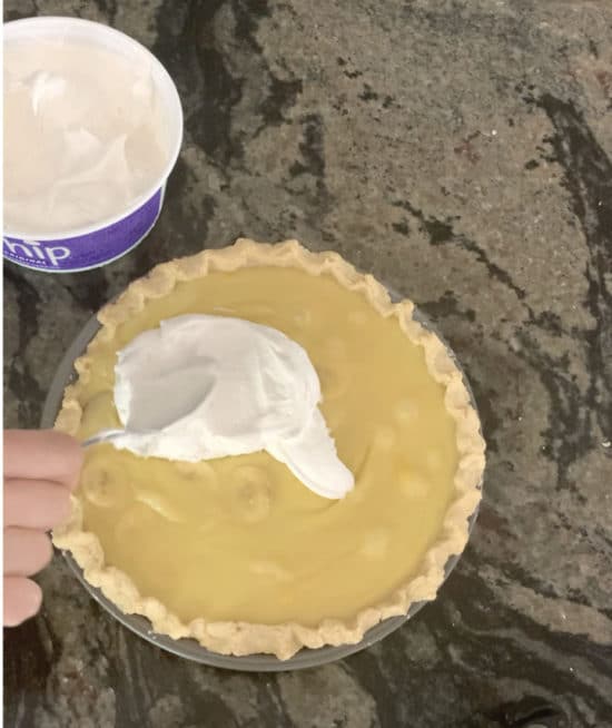 Spreading whipped cream over the banana cream pie.