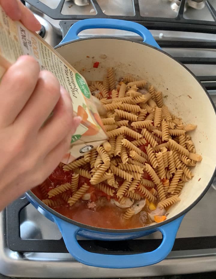 Pouring chicken broth over the dry pasta.