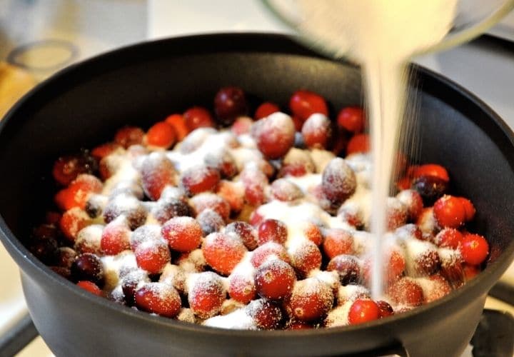 Pouring sugar into cooking cranberries.