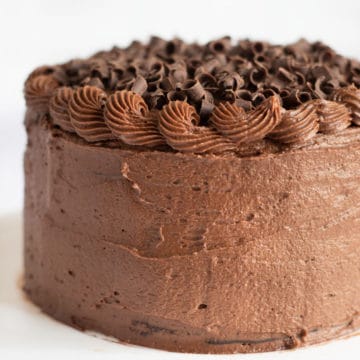 A whole chocolate frosted cake on a white plate.