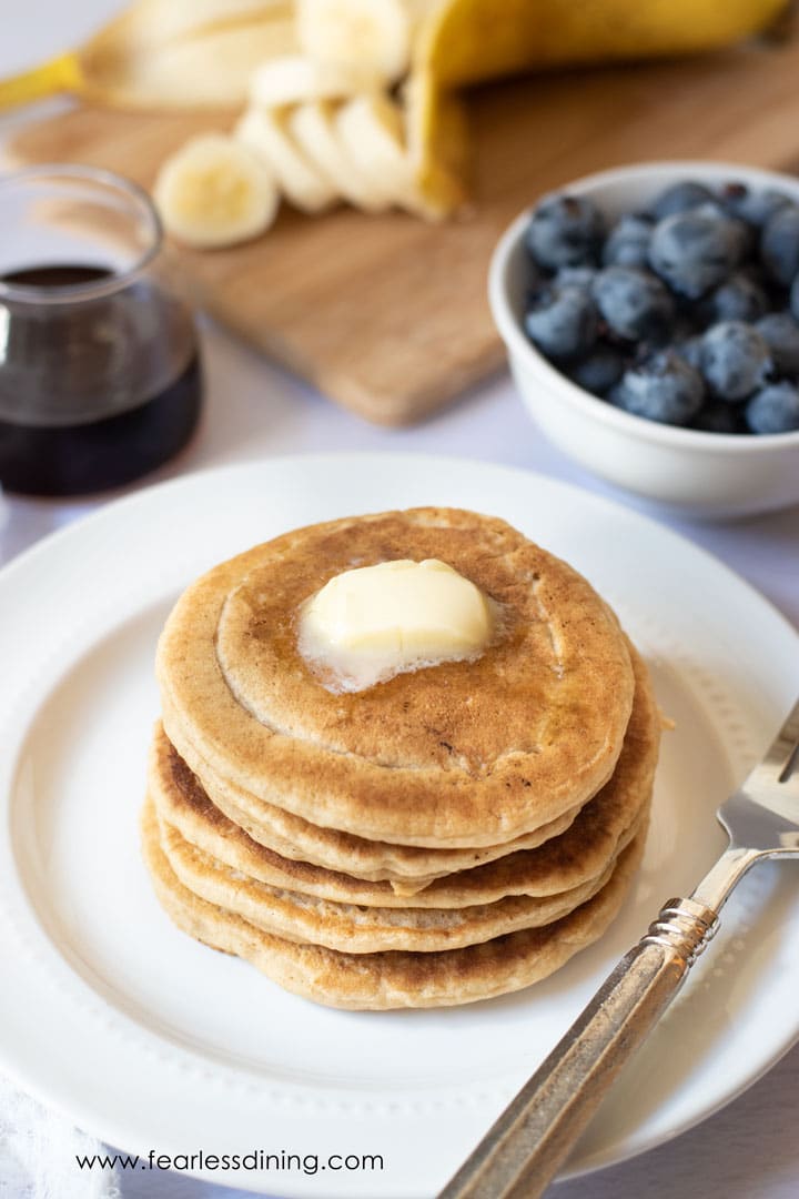 A stack of gluten free pancakes on a plate. There is a wedge of butter on top.