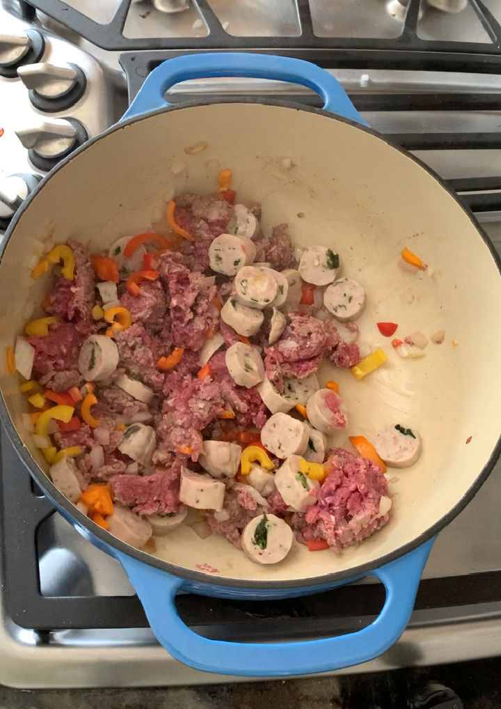 Cooking the ground beef, onion, garlic, peppers, and sausage in a big pot.