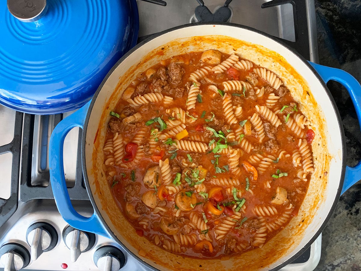 A blue cast iron Dutch oven full of one pot tomato basil pasta.