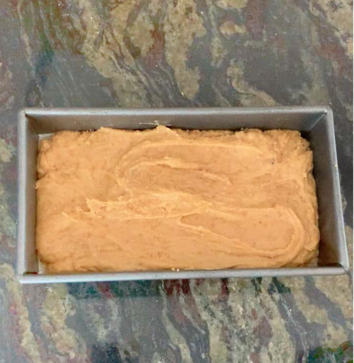 A loaf tin filled with pumpkin bread batter.