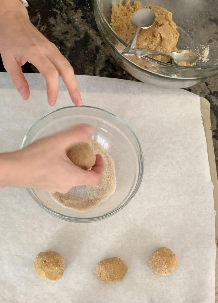Rolling cookie dough balls in sugar and cinnamon.