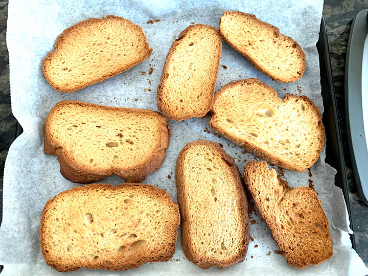 Baked dried bread slices on a baking tray.
