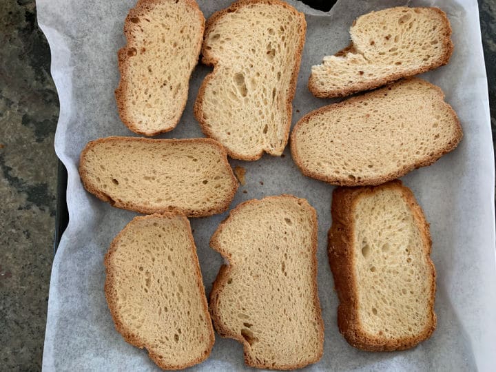 Gluten free bread slices on a parchment paper lined baking sheet.