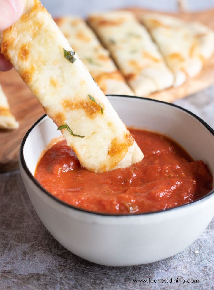 Dipping a gluten free flatbread slice in marinara sauce.