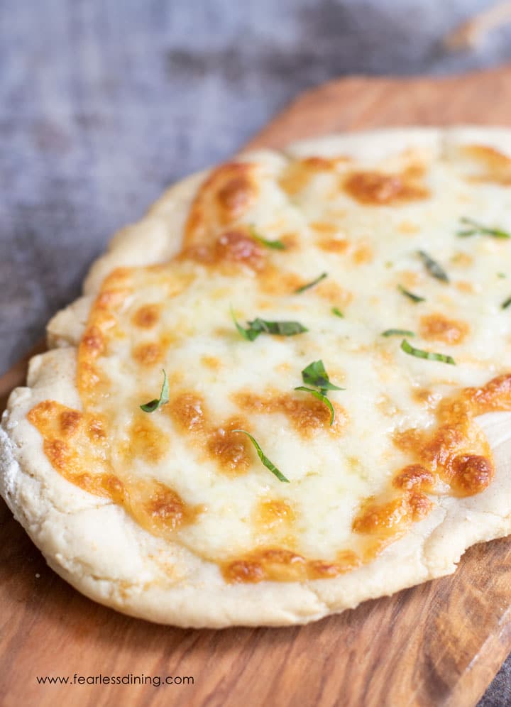 A whole flatbread topped with mozzarella cheese on a cutting board.