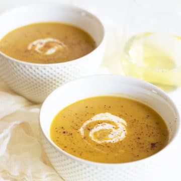 Two bowls of butternut squash soup. They are garnished with cream.