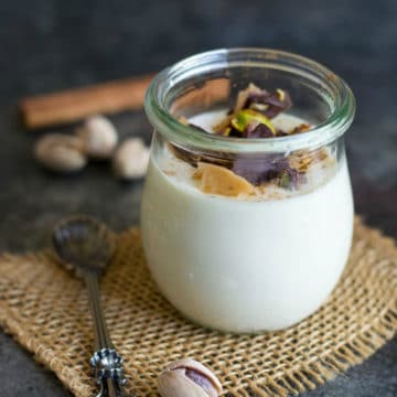 A fancy glass filled with eggnog panna cotta. It is garnished with crushed pistachio toffee.