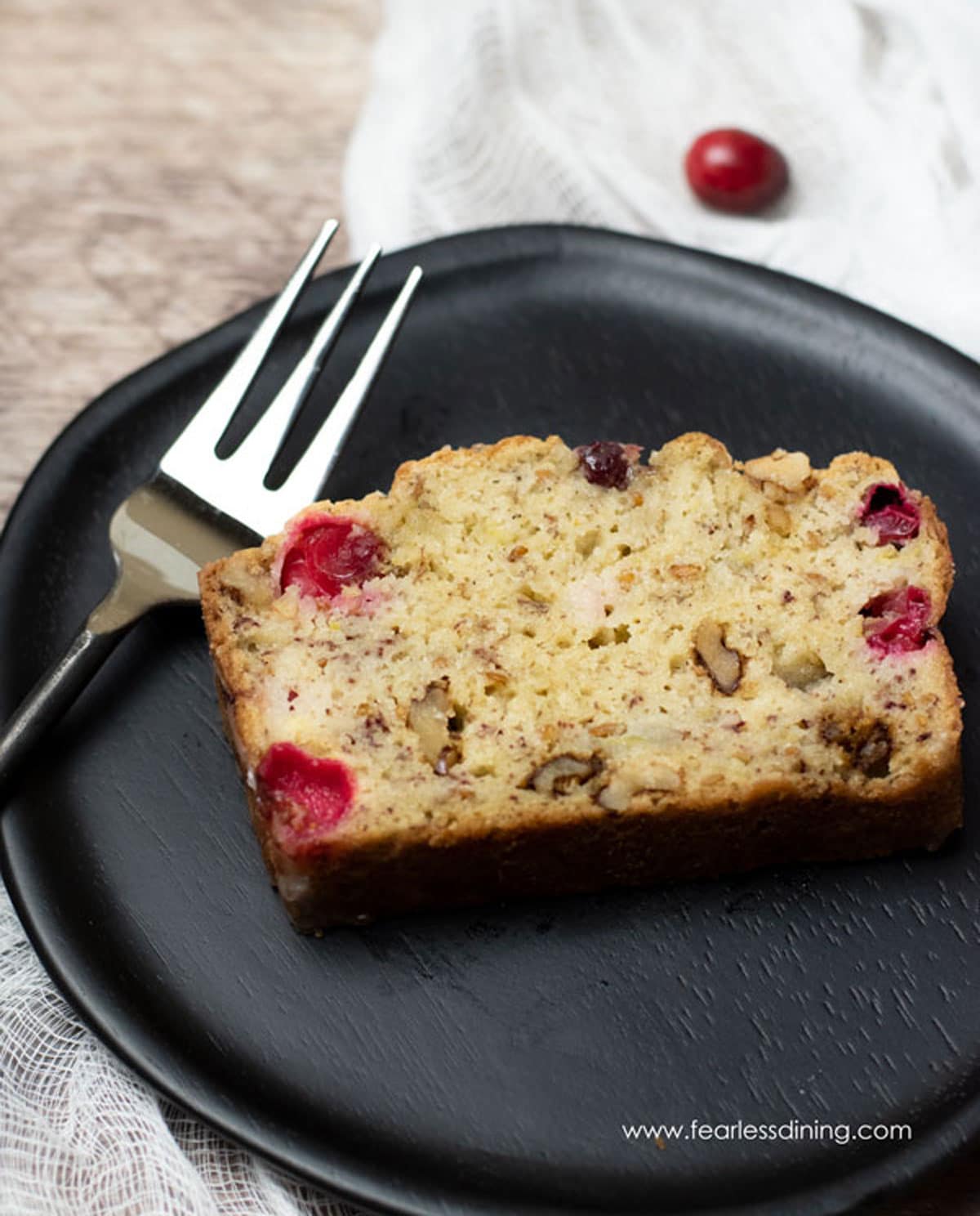 A slice of cranberry banana bread on a wooden plate.