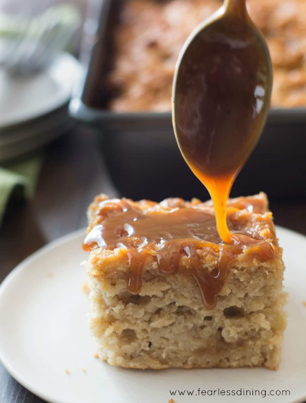 A spoon drizzling caramel over a slice of apple cake.