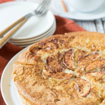 A big apple cake on a plate next to an espresso.