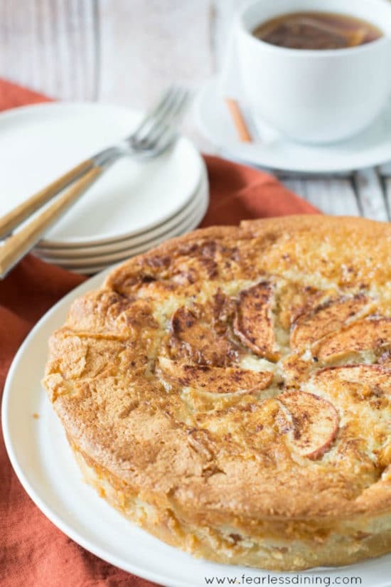 A big apple cake on a plate next to an espresso.