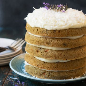 A fancy carrot cake with cream cheese frosting. The cake is topped with shredded coconut and a lavendar flower.