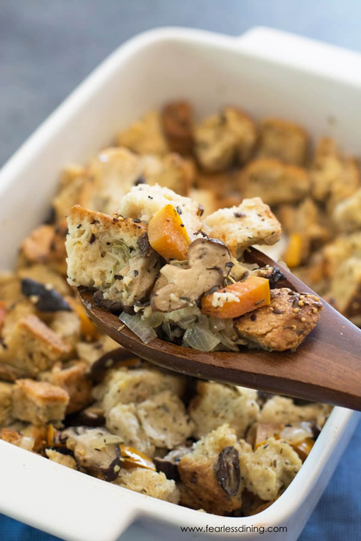 A casserole dish full of dressing. A serving spoon is holding up a serving.