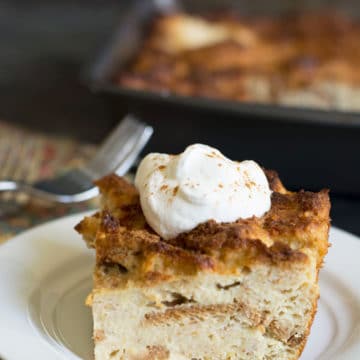 A slice of eggnog bread pudding on a plate. It has a small dollop of whipped cream.