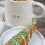 A gingerbread biscotti on a plate next to a mug of coffee.