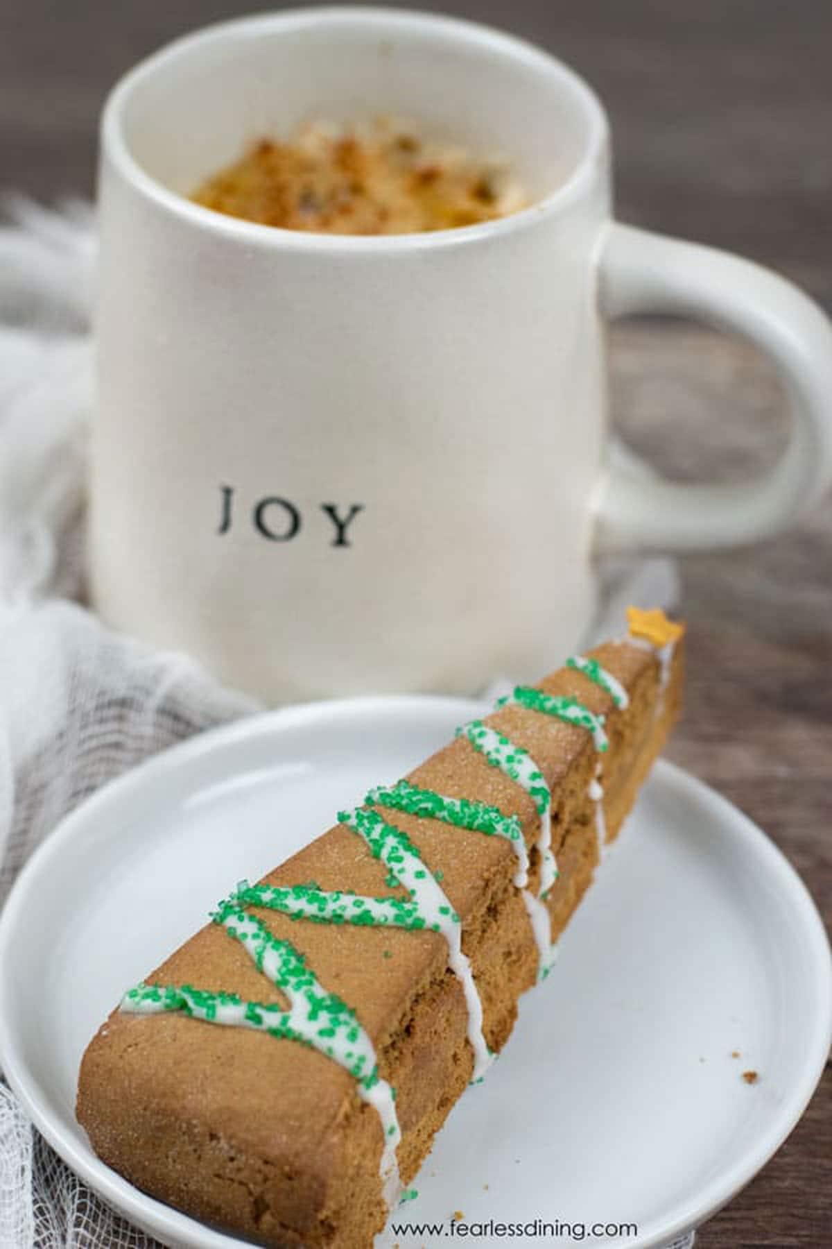 A gingerbread biscotti on a plate next to a mug of coffee.