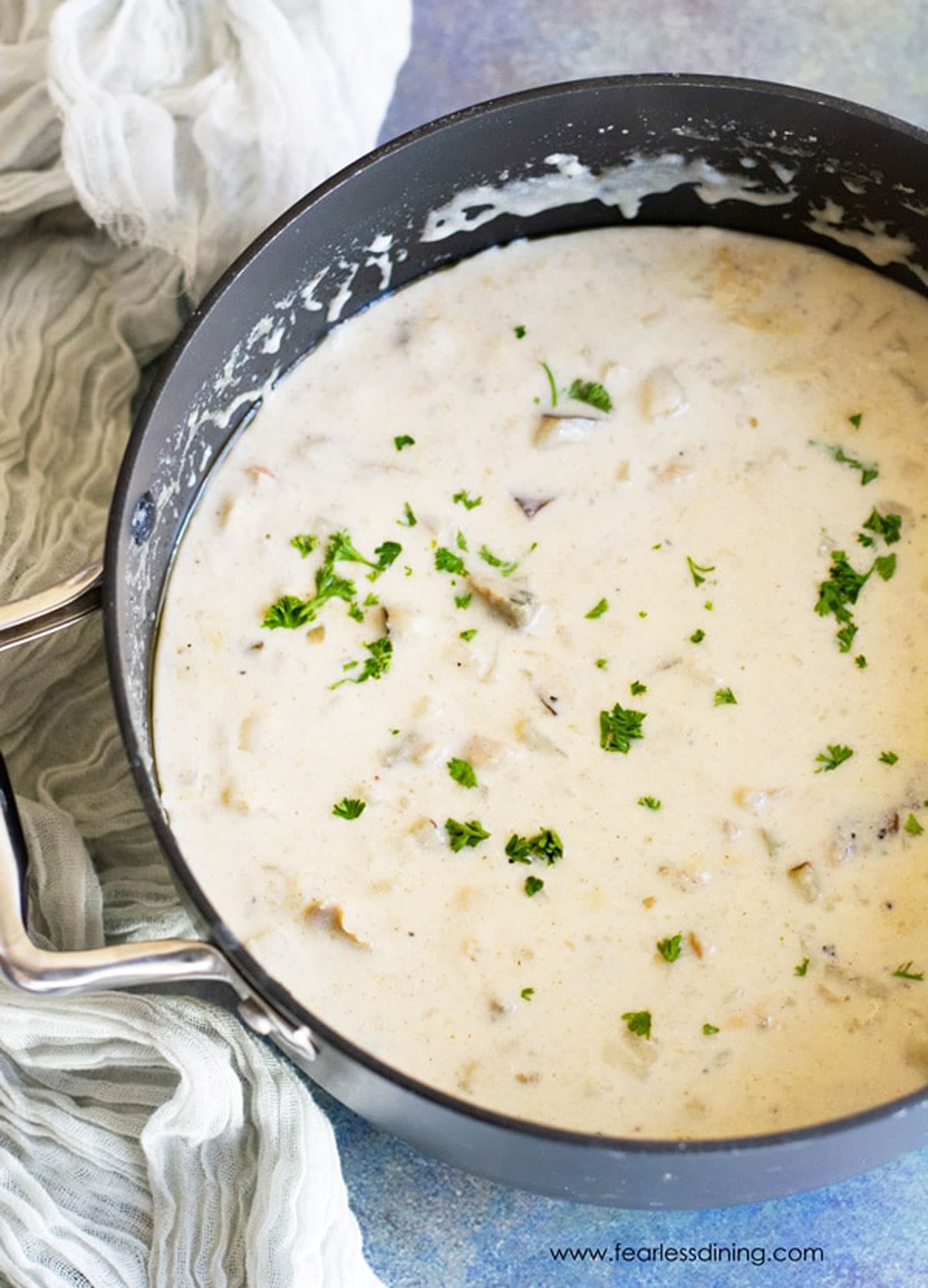 A big pot of cooked clam chowder. It is garnished with fresh chopped parsley.