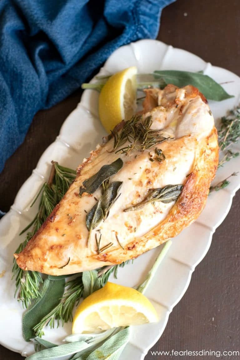 A close up photo of a roasted turkey breast on a platter. It has fresh herbs around the meat.