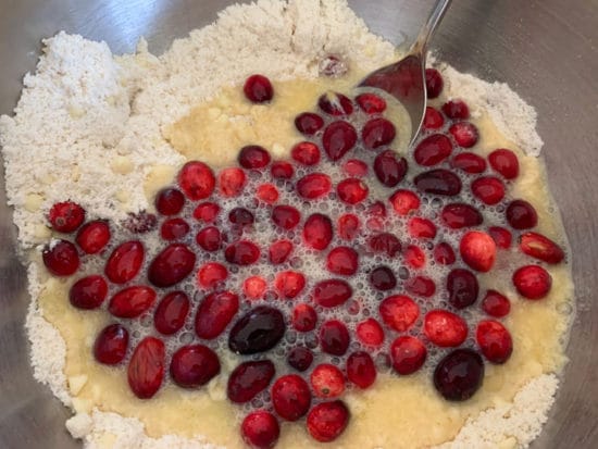 The wet and dry ingredients in a bowl with the fresh cranberries.