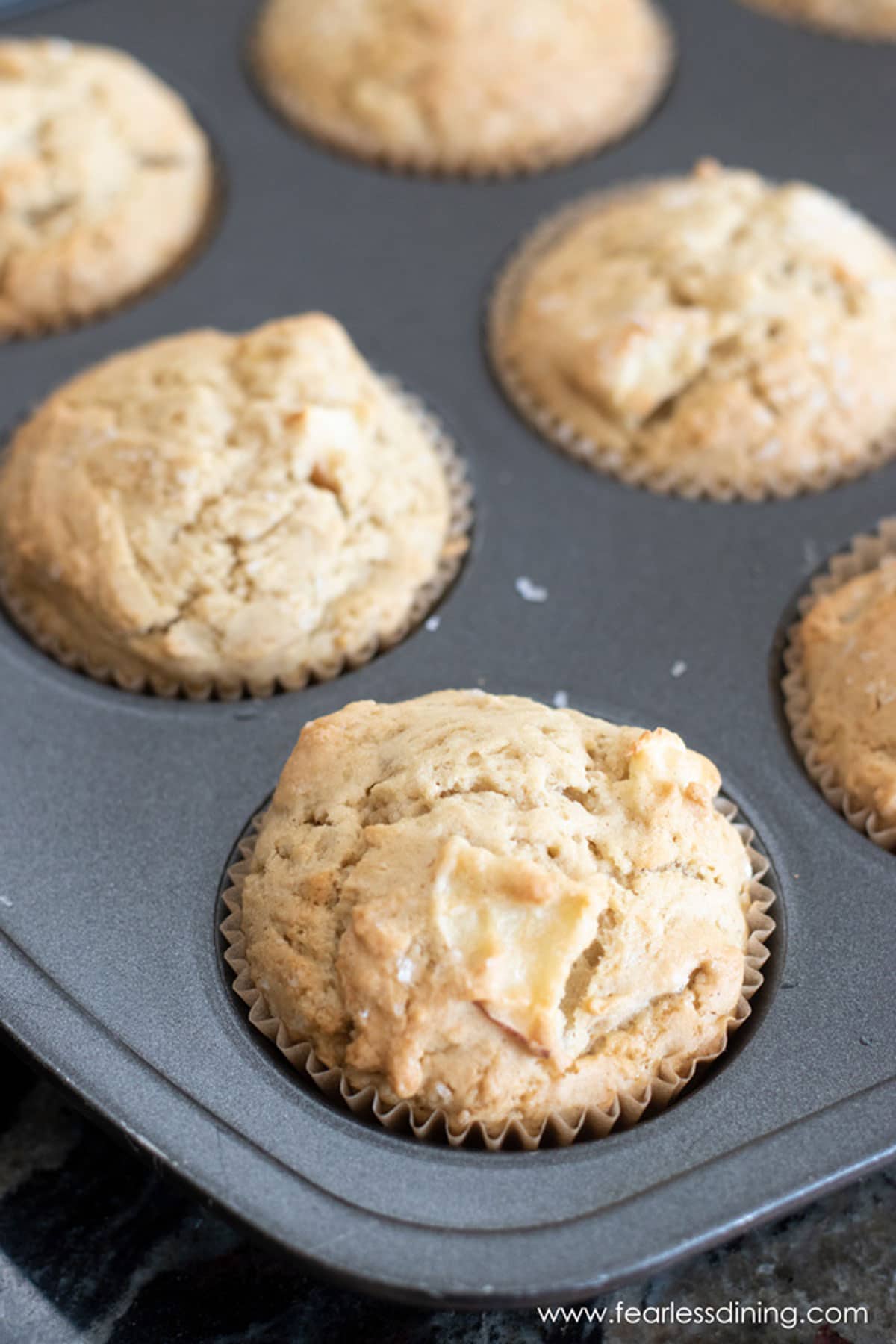 A muffin tin full of baked apple muffins.
