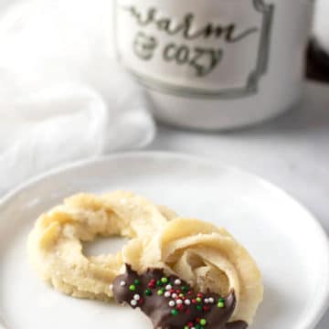 Two butter cookies on a plate next to a coffee mug.