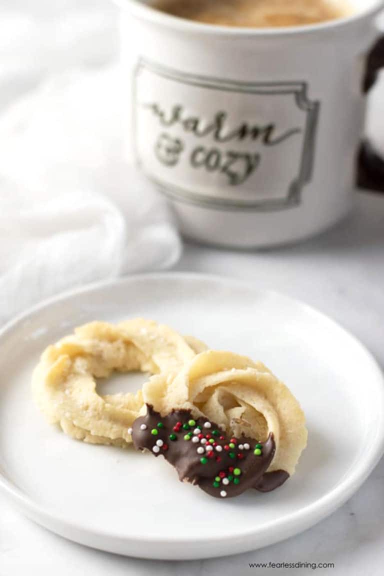 Two butter cookies on a plate next to a coffee mug.