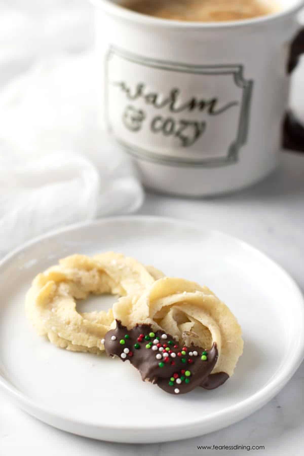 Two butter cookies on a plate next to a mug of coffee.