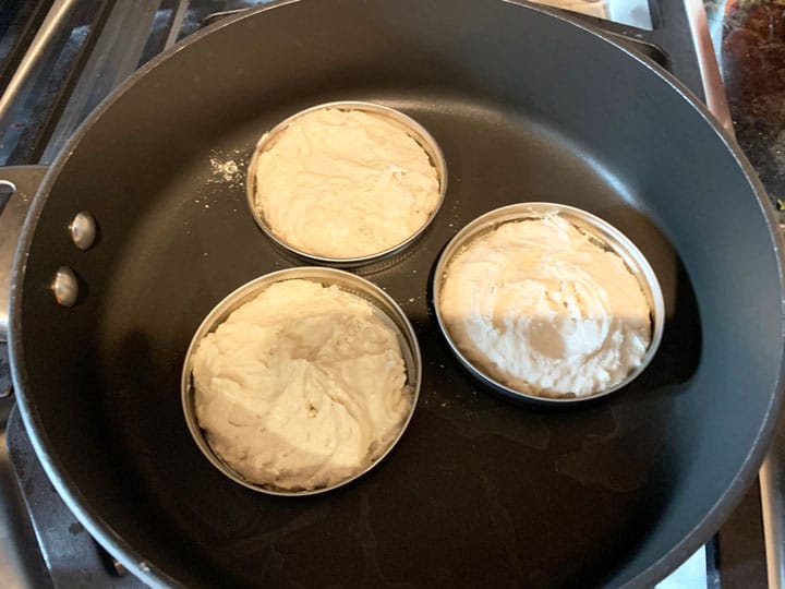 Three English muffins in round molds cooking on a skillet.