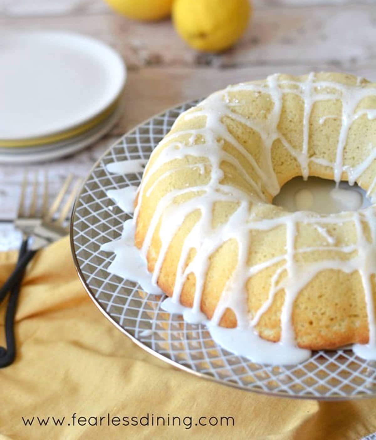 A lemon bundt cake on a cake stand. The cake has lemonade icing drizzled over the top.