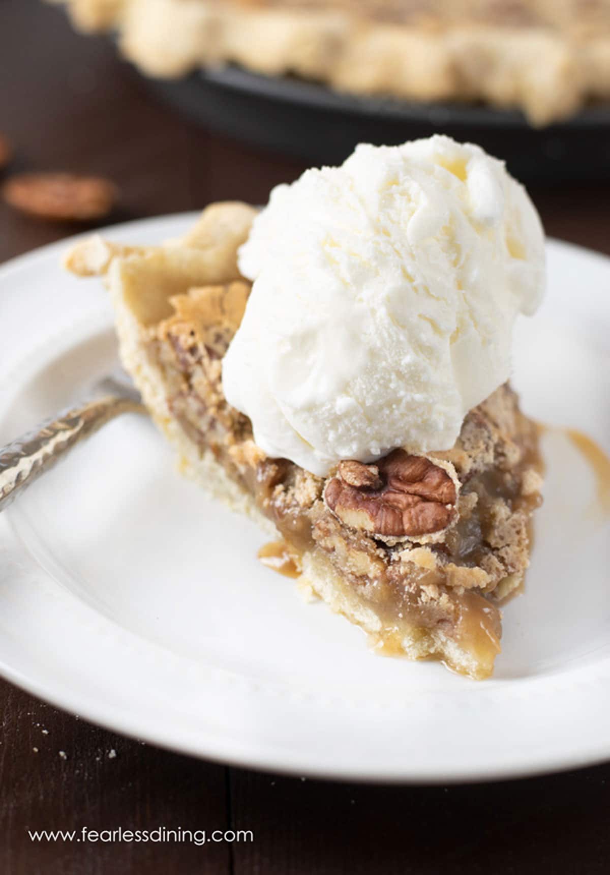 A slice of pecan pie topped with a scoop of vanilla ice cream.