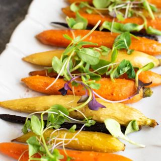 A platter with whole maple roasted carrots, topped with sprouts.