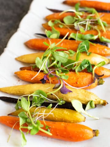 A platter with whole maple roasted carrots, topped with sprouts.