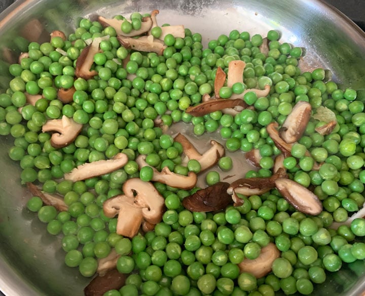 Peas and shiitake cooking together in a pan.